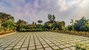 A paved outdoor area with a grid pattern, surrounded by lush greenery and trees. - Hirkani Garden & Resort (Mahabaleshwar)