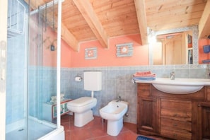 Une salle de bain avec douche, deux toilettes, un bidet, un lavabo et des meubles de rangement en bois.
