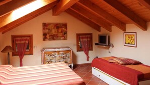 Une chambre confortable située sous les toits, avec des poutres apparentes, un lit, une commode et des œuvres d’art accrochées aux murs.
