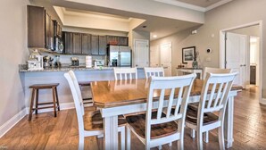 A modern kitchen with dark cabinets, a central island, and a dining area with white chairs and a wooden table. - Private Balcony! Free Activities! Walk to Beach! Gated Community Alerio B205 (Destin)