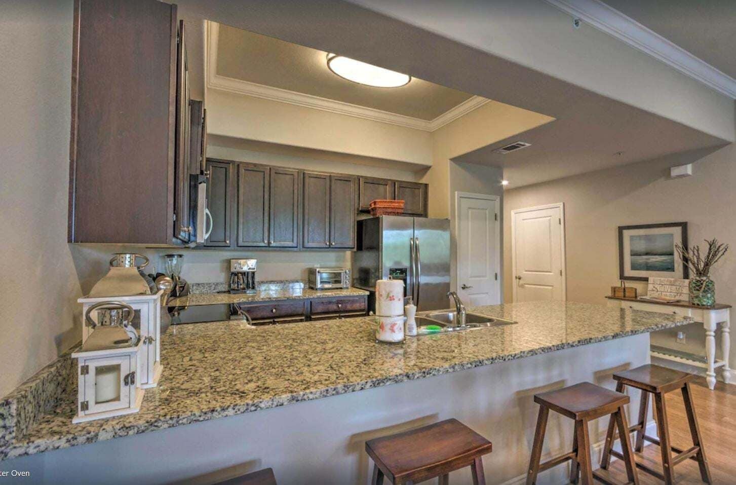 A kitchen with granite countertops, dark wooden cabinets, a stainless steel refrigerator, and a built-in oven.