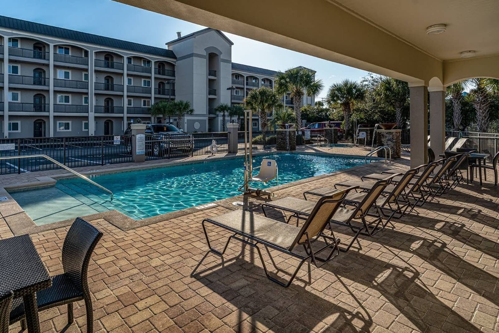 A poolside area with lounge chairs and a swimming pool, surrounded by a building with multiple balconies and palm trees.