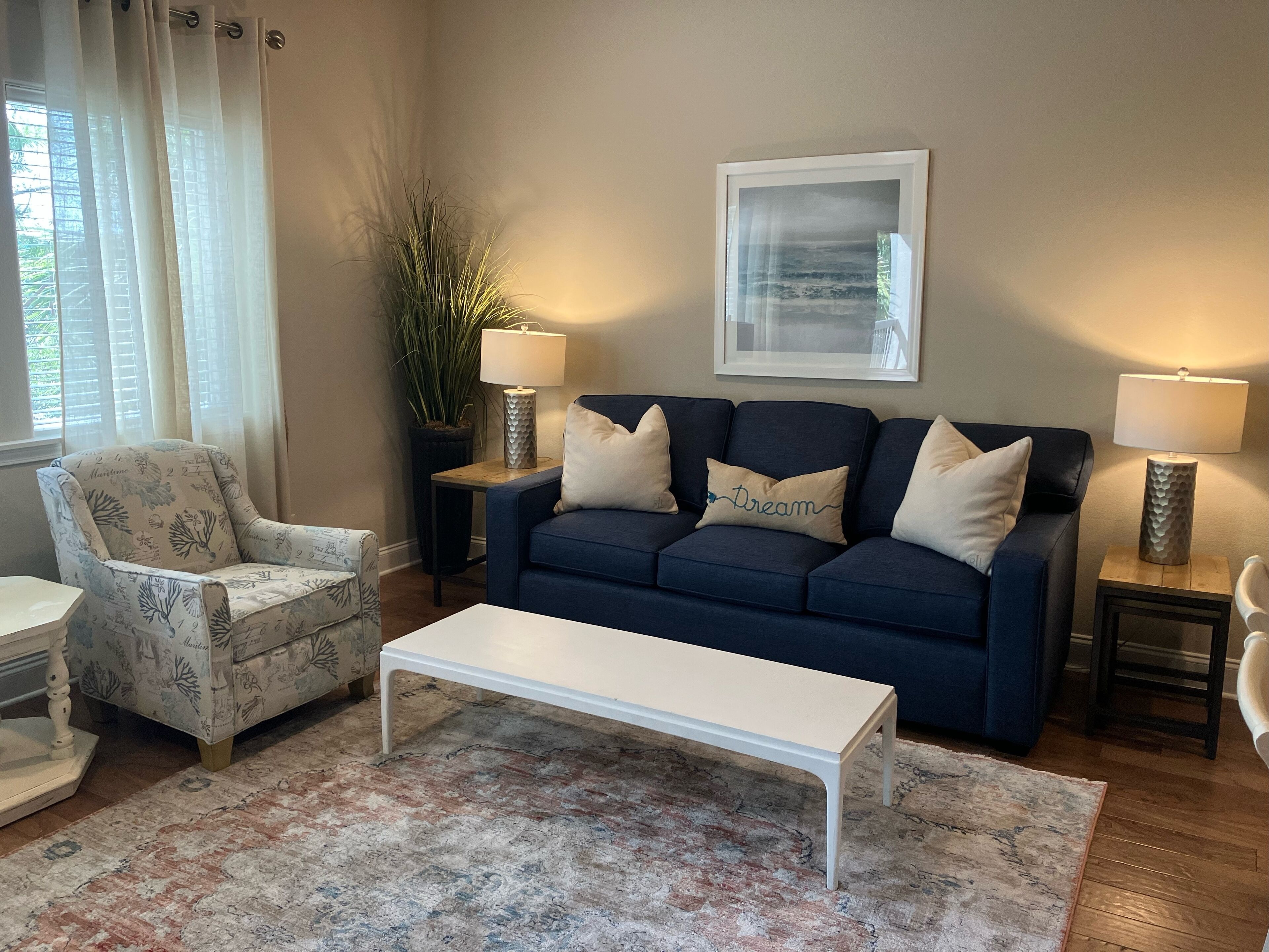 Un salon avec un canapé bleu, une table basse blanche, un fauteuil à motifs, une plante en pot et un tableau encadré accroché au mur.