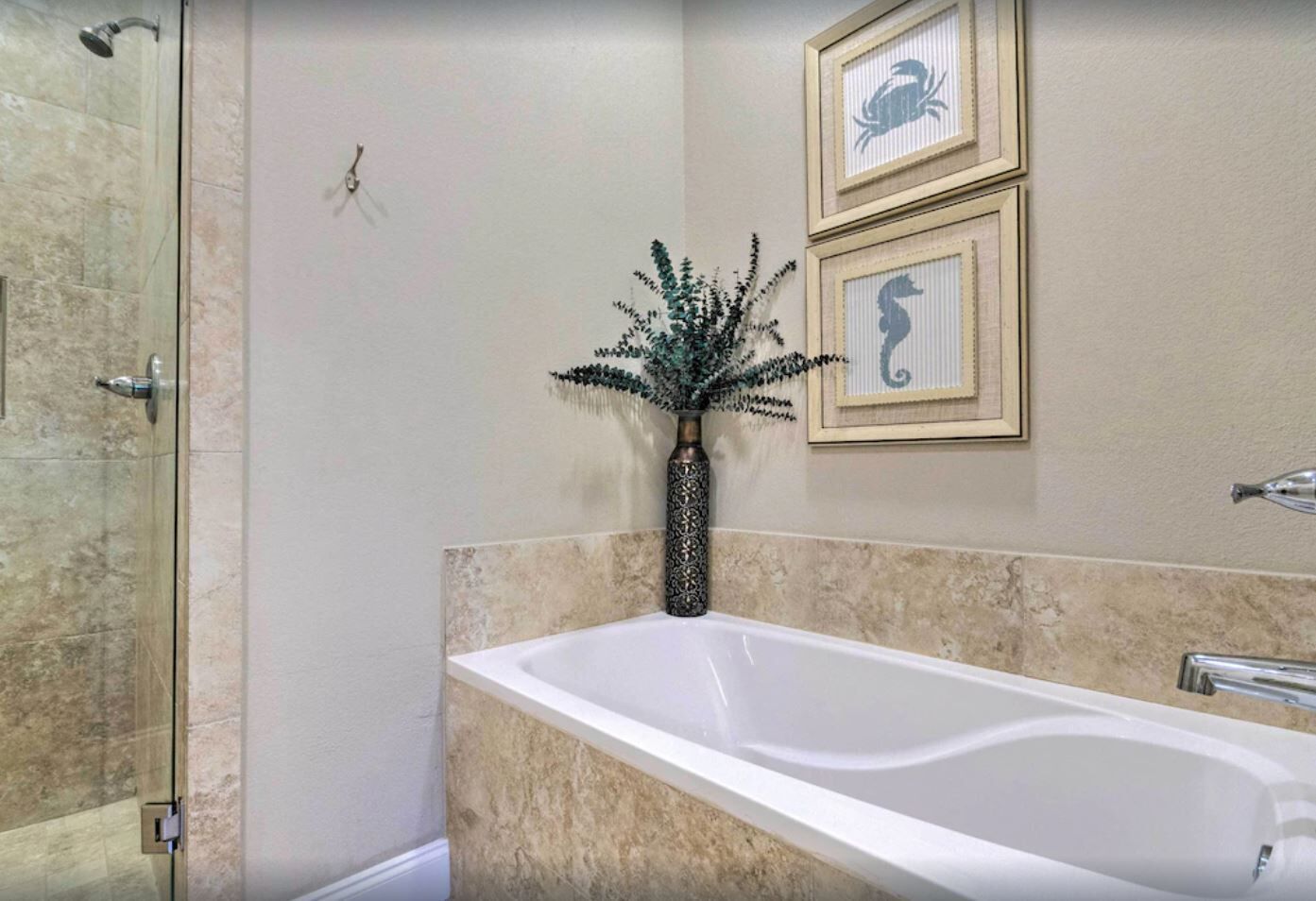 A bathroom with a glass-enclosed shower, a white bathtub, and framed artwork on the wall.