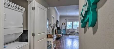 A hallway with a laundry room on the left, a dining area with a table and chairs in the center, and a wall with a decorative sign on the right.