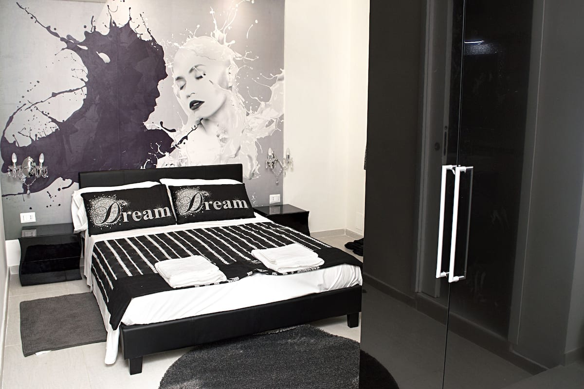 A modern bedroom with a black and white color scheme, a large bed with two pillows, a nightstand, and a wall mural.