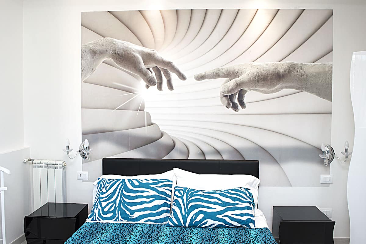 A modern bedroom with a bed centered under a large mural of hands reaching towards each other.
