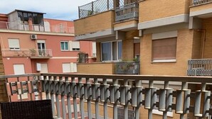 Un balcon avec deux petites tables rondes en verre et des chaises, une rambarde en métal et un sol carrelé.