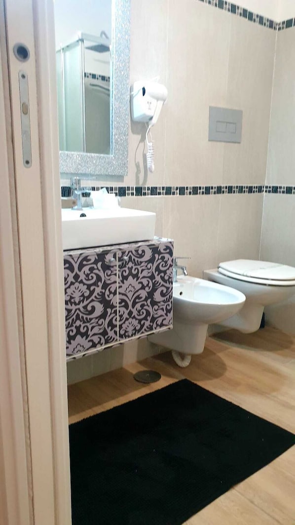 Casa de banho com lavatório branco, espelho, sanita e móvel com padrão.