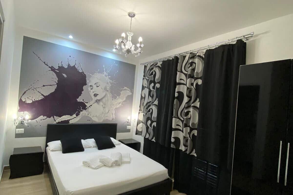 A modern bedroom with a large bed, a black and white patterned curtain, a black wardrobe, and a wall mural.