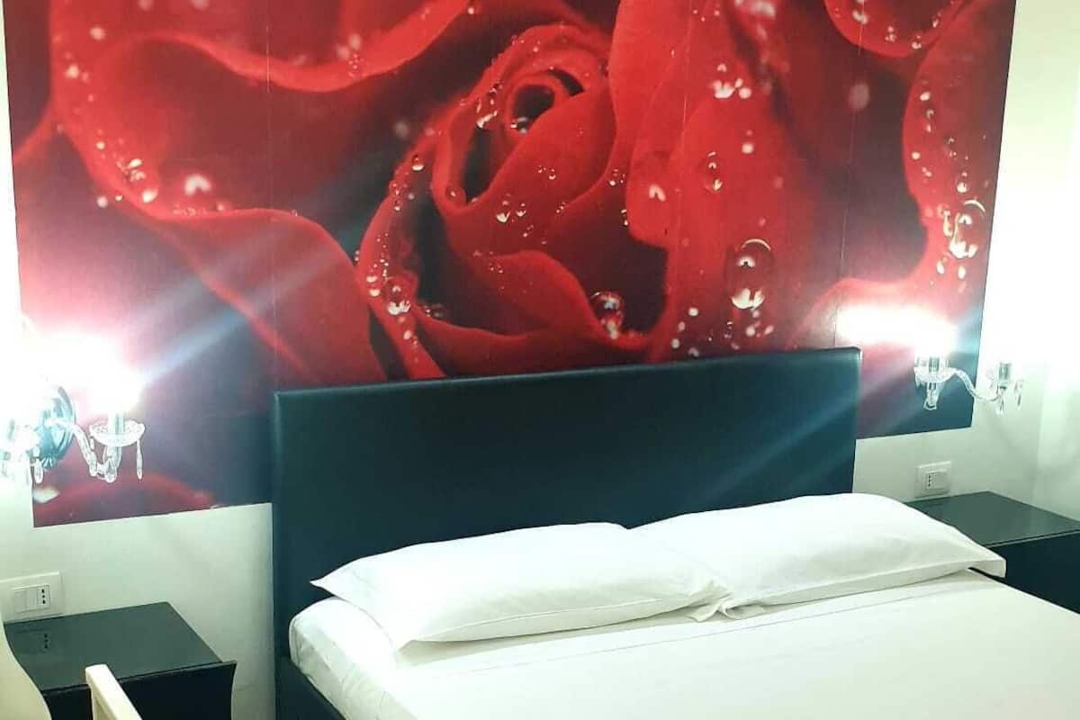 A bedroom with a large bed, a red rug, a white ladder, and a wall-mounted TV displaying a red rose.