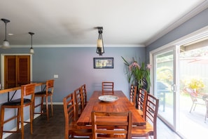 Un espace repas comprenant une table et des chaises en bois, un luminaire suspendu et une grande fenêtre donnant sur l’extérieur.