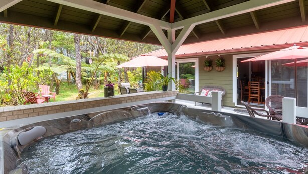 A hot tub area with a covered patio, outdoor furniture, and lush greenery visible through the windows. - Lovely, Spacious Villa with HotTub, Outdoor Dining, Fire Pit (Volcano)