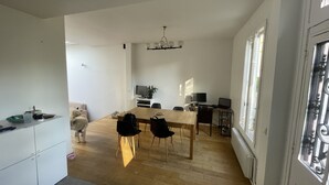 Àmplia zona d'estar amb una taula de dinar de fusta, dues cadires, un sofà i una televisió.