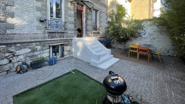 Un pati amb una barbacoa, seients exteriors i una escala que porta a l'entrada d'un edifici.