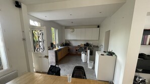 Una cuina moderna amb armaris blancs, una taula de menjador amb un calador i un menú, i vista cap a la zona de sala adjacent.