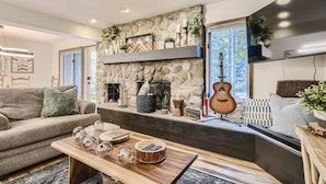 Una sala de estar acogedora con chimenea de piedra, un sofá, una mesa de centro con objetos decorativos y una guitarra.