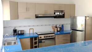 Una cocina moderna con armarios de tonos claros, una encimera azul, un refrigerador de acero inoxidable, una estufa y un microondas.