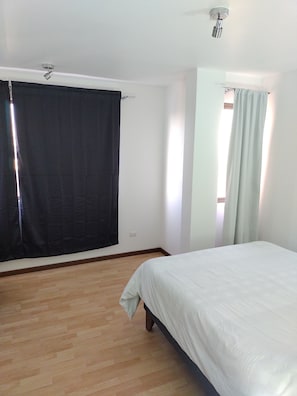 Un dormitorio con cama, suelo de madera, ventilador de techo y ventana con cortinas.