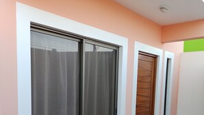 Un pasillo con amplios ventanales correderos y una puerta de madera, que conduce a una habitación con suelo de baldosas.