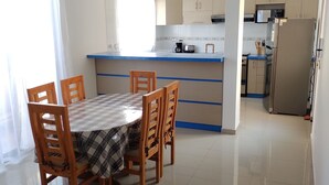 Una cocina moderna con encimera azul, una mesa de comedor con sillas de madera y un refrigerador.