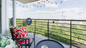 A balcony with a chair, a small table, and a view of a green area beyond a fence. - Comfortable Apartment | Pool Access and Balcony (Poznań)