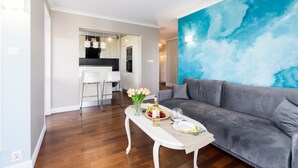 A modern living room with a grey sofa, a white coffee table with a vase of flowers, and a blue abstract wall. - Comfortable Apartment | Pool Access and Balcony (Poznań)