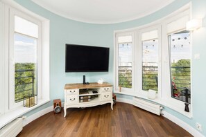 Une pièce dotée d’un grand téléviseur à écran plat fixé au mur, d’un meuble de rangement en bois et offrant une vue dégagée grâce à de grandes fenêtres.