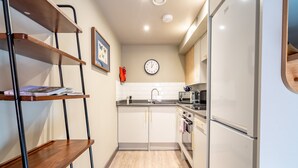 A compact kitchen with white cabinets, a microwave, a sink, and a clock on the wall. - The Falcon Apartment 6 (York)