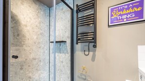 A modern bathroom with a glass shower enclosure, a towel rack, and a sign that reads "It's a Yorkshire thing". - The Falcon Apartment 6 (York)