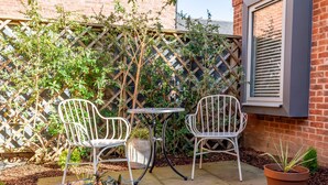 A patio with two white metal chairs and a small table, surrounded by a wooden lattice fence and potted plants. - The Falcon Apartment 6 (York)