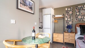 A compact room with a bed, a small table with chairs, a wardrobe, a refrigerator, and a wall with floral wallpaper. - The Falcon Apartment 7 (York)