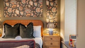 A hotel room with a bed, a nightstand, a lamp, and a wall with floral wallpaper. - The Falcon Apartment 7 (York)