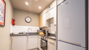 A modern kitchen with white cabinets, a stainless steel refrigerator, a microwave, and a clock on the wall. - The Falcon Apartment 7 (York)