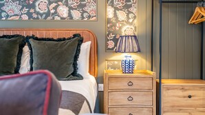 A bedroom with a bed, two bedside tables, a lamp, and a wall with floral wallpaper. - Studio - Sleeps 2 Guests (York)