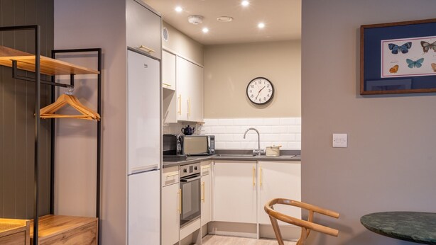 A compact kitchen with white cabinets, a microwave, a sink, and a clock on the wall. - Studio - Sleeps 2 Guests (York)