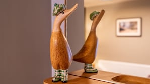 Une figurine en bois représentant un canard, portant un chapeau et des bottes à carreaux, posée sur une surface en bois.