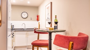 Une cuisine moderne avec des meubles blancs, un évier et une horloge au mur. On y trouve une table avec deux chaises et une bouteille de vin.