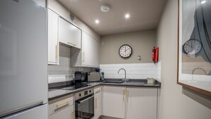 Une cuisine moderne avec des armoires blanches, des appareils en acier inoxydable, un four à micro-ondes et une horloge murale.