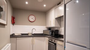 A modern kitchen with white cabinets, a black countertop, a microwave, a kettle, and a refrigerator. - The Falcon Tap Apartment 2 (York)