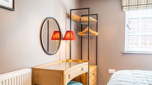 A bedroom with a wooden vanity, a mirror, two red lamps, a blue stool, and a bed with a white quilt. - The Falcon Tap Apartment 2 (York)