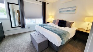 Een hotelkamer met een groot bed, twee nachtkastjes met lampen, een raam met gordijnen, een spiegel en een schilderij aan de muur.