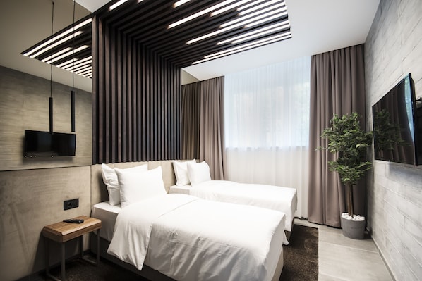 Una habitación de hotel moderna con dos camas, televisión y un gran ventanal con cortinas.