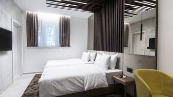 Ein modernes Hotelzimmer mit einem großen Bett, einem Nachttisch mit Fernbedienung, einem gelben Sessel und einem großen Spiegel.