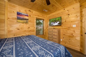 Una camera in una baita di legno con un letto, una cassettiera, una televisione e due quadri appesi alle pareti.