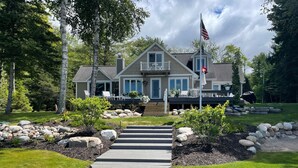 Uma casa de dois andares com varanda frontal, um mastro com a bandeira americana e um caminho de pedra que leva à entrada.