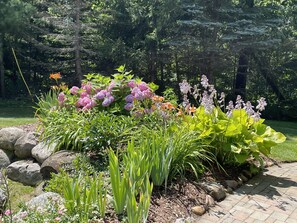A garden with various plants and flowers, a paved walkway, and a stone border. - Lake Michigan Getaway  (Charlevoix)