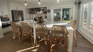 Uma cozinha moderna com ilha central, eletrodomésticos de aço inoxidável, cadeiras de vime, iluminação pendente e vista para o exterior.