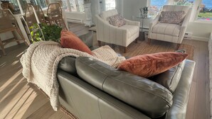 A living room with a leather sofa, two armchairs, a dining table with chairs, and large windows with a view of the ocean. - Lake Michigan Getaway  (Charlevoix)