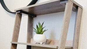 Une étagère en bois à trois niveaux, sur laquelle sont posés un vase blanc et une plante en pot, sur l’étagère supérieure.